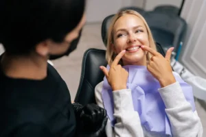 Close-up top view of happy young woman patient pointing with fingers at healthy smile, demonstrating whitening teeth procedure result, satisfied with dental clinic service. Concept of dental treatment