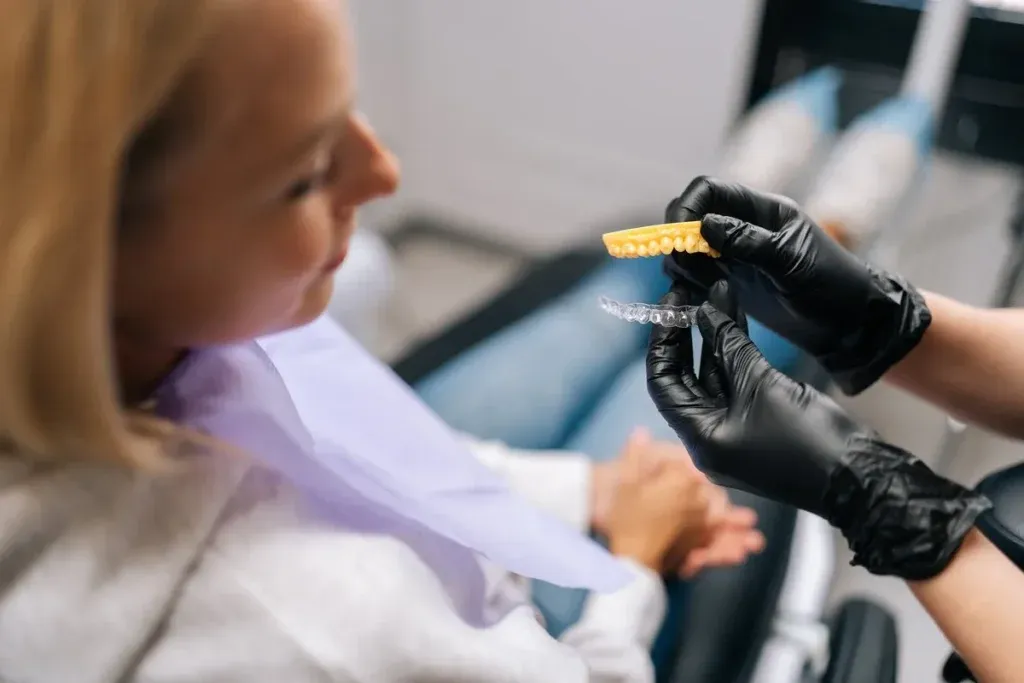 Close-up high-angle view of unrecognizable orthodontist in gloves showing aligners to young woman patient during consultation at dental clinic. Concept of stomatology, dentistry and orthodontics