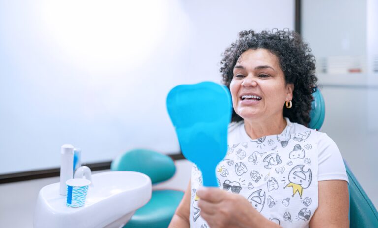 Smiling patient admiring her smile with a hand mirror in an Aqua Dentistry treatment room